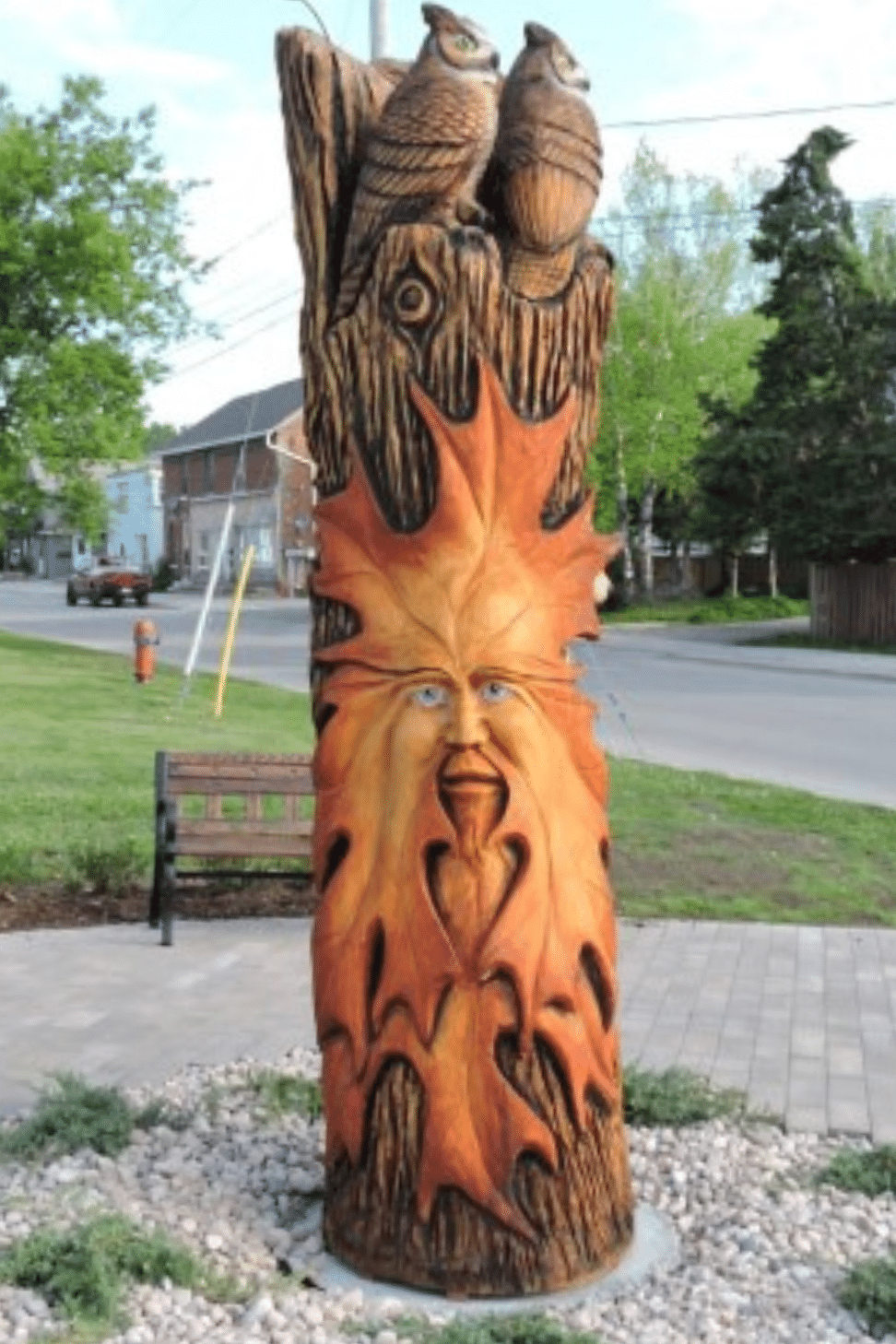 Tree sculpture with a large leaf with a face inside of it carved into the side of the trunk